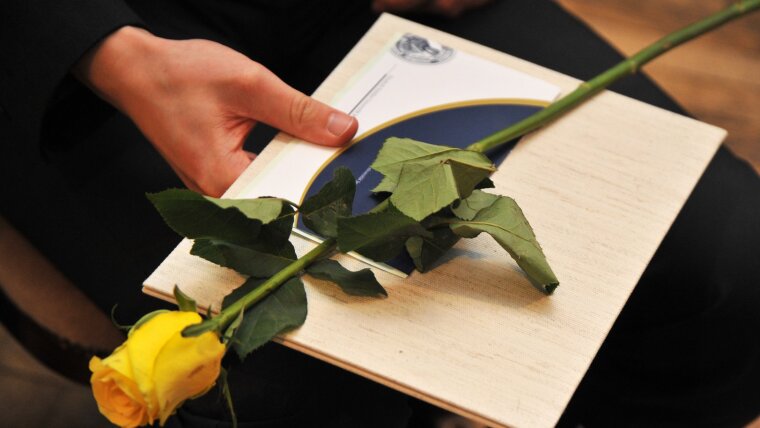 A graduate holds a diploma and a rose in his hand.