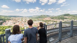 Drei Studierende blicken vom JenTower ins Saaletal und auf die Stadt Jena.